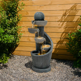 Elegante elektrische Wasseranlage "Spiral Springs" aus schwarzem Stein, mit mehreren Wasserschalen, die sanft über die Stufen fließen, umgeben von grünen Pflanzen