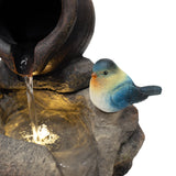 Eine elektrische Wasseranlage mit einem rustikalen Topf, aus dem Wasser fließt, und einem bunten Vogel aus Kunststein auf einer steinernen Oberfläche