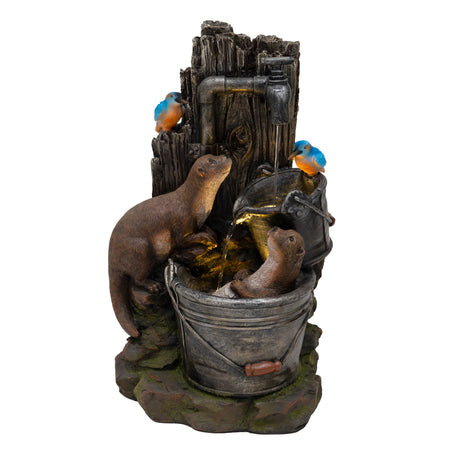 Zwei spielende Otter in einer rustikalen Wasseranlage mit Holz- und Metalldetails, umgeben von bunten Vögeln und grünem Moos