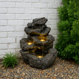 Rustikale Wasseranlage "Rustic Rapids" aus steinähnlichem Material mit drei Ebenen, sanft fließendem Wasser und integrierten LED-Lichtern in einem Gartenumfeld