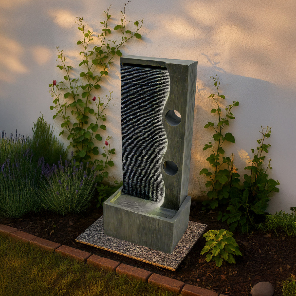 Elegante elektrische Wasseranlage "Harmony Falls" aus grauem Stein mit sanft fließendem Wasser, umgeben von grünen Pflanzen und Lavendel
