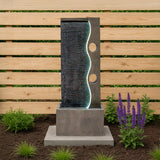 Moderne elektrische Wasseranlage "Harmony Falls" mit sanft fließendem Wasser, beleuchtetem Wellenmuster und grauem Beton, umgeben von lila Blumen und grünem Gras