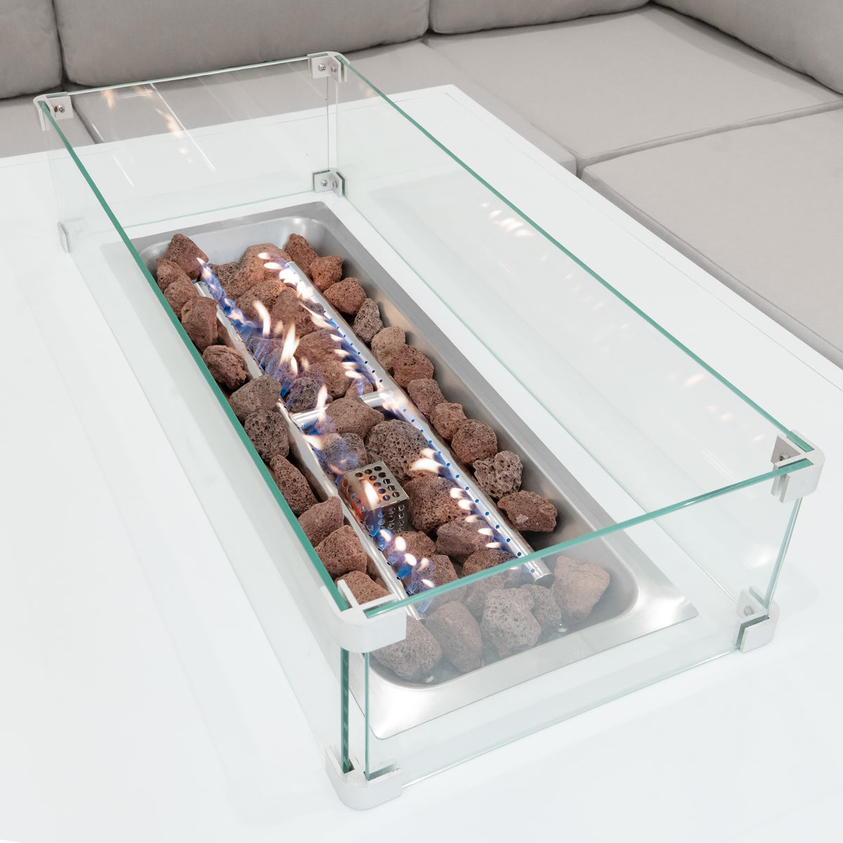 Modulares Gartenmöbelset aus weißem Aluminium mit einer eleganten Feuerstelle, umgeben von dekorativen Steinen und einem klaren Glasrahmen