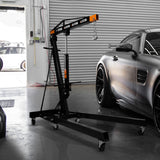 Schwarzer 1-Tonnen-Motorkran mit stabiler Basis und Rollen, neben einem sportlichen Auto in einer modernen Werkstatt, ideal für Hebe- und Reparaturarbeiten