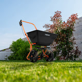 Rasennivellierer und Rotationsstreuer von T-Mech in Grün mit orangefarbenem Gestell, großen Rädern und robustem, schwarzem Behälter auf grünem Rasen