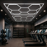 Zehn hexagonale LED-Leuchten in modernem Design, strahlend weiß, an der Decke eines stilvollen Fitnessstudios über Laufbändern montiert