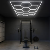 Zehn hexagonale LED-Leuchten in modernem Design, montiert an einer dunklen Decke über einem Fitnessbereich mit Hantelbank und Gewichten