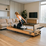 Pilates Reformer Maschine aus Eiche, elegant und modern, mit einer Person in sportlicher Kleidung, die eine Übung ausführt, im hellen Raum