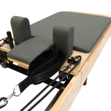 Pilates Reformer Maschine aus Eiche mit grauem Polster, gepolsterten Kopfstützen und verstellbaren Widerstandsbändern für vielseitiges Training