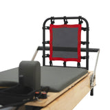 Pilates Reformer Maschine aus Eiche mit schwarzem Rahmen, grauem Polster und rotem elastischen Band, ideal für effektives Training und Komfort
