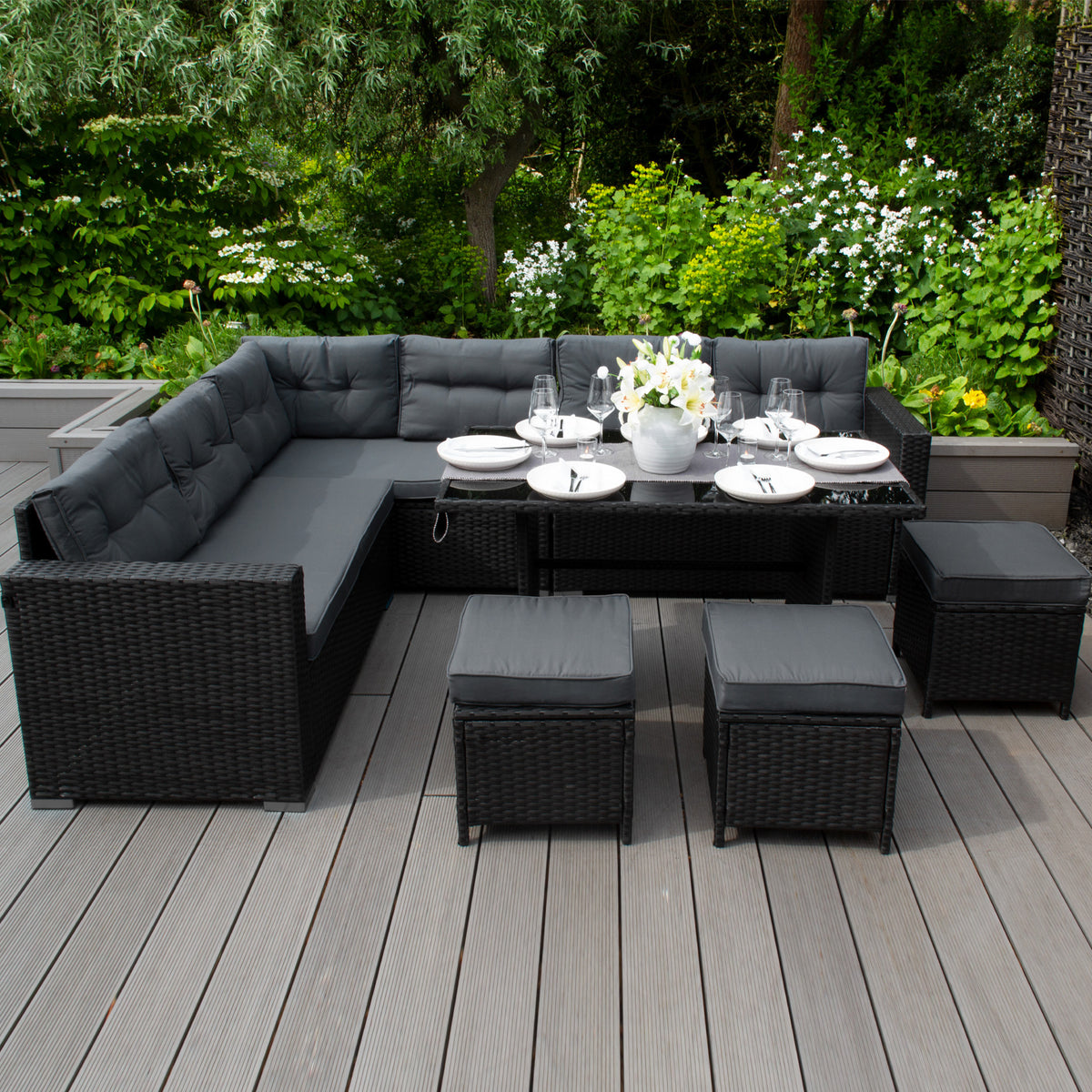 Schwarze Gartenmöbel mit gepolsterten Kissen, eleganter Essbereich im Freien, umgeben von grünen Pflanzen und Blumen, stilvoll und modern
