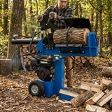 Der 15T Holzspalter in leuchtendem Blau, robust und leistungsstark, spaltet einen großen Baumstamm in einer herbstlichen Waldumgebung mit Holzstapeln im Hintergrund