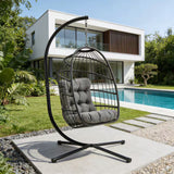 Schwarzer Rattan Hängesessel in Eiform mit grauem Kissen, elegant aufgehängt an einem stabilen Gestell, umgeben von einem modernen Garten und Pool