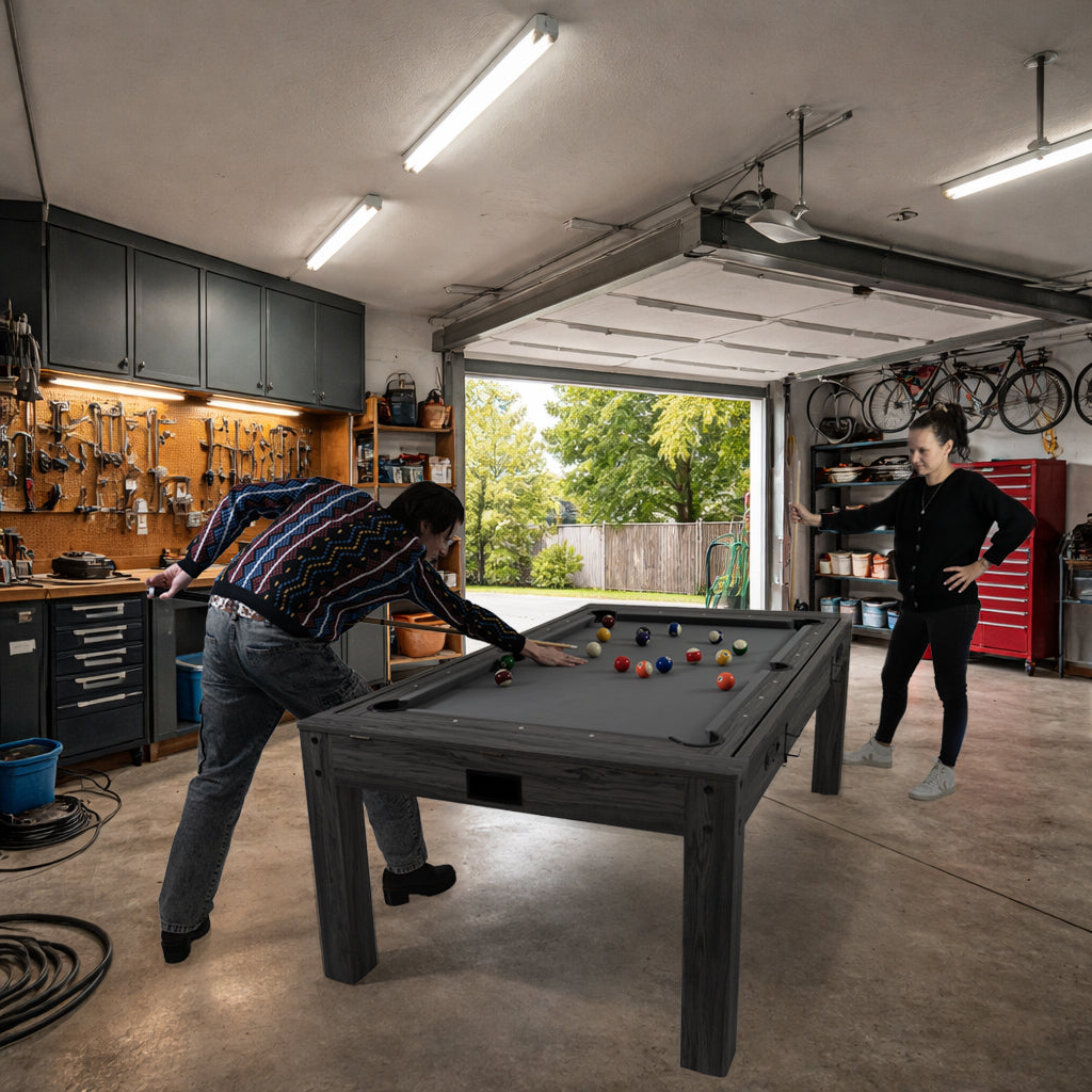 Zwei Personen spielen an einem grauen 7-in-1 Spieltisch mit LED-Ringlicht in einer gut beleuchteten Garage, umgeben von Werkzeugen und Fahrrädern