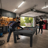 Zwei Personen spielen an einem grauen 7-in-1 Spieltisch mit LED-Ringlicht in einer gut beleuchteten Garage, umgeben von Werkzeugen und Fahrrädern