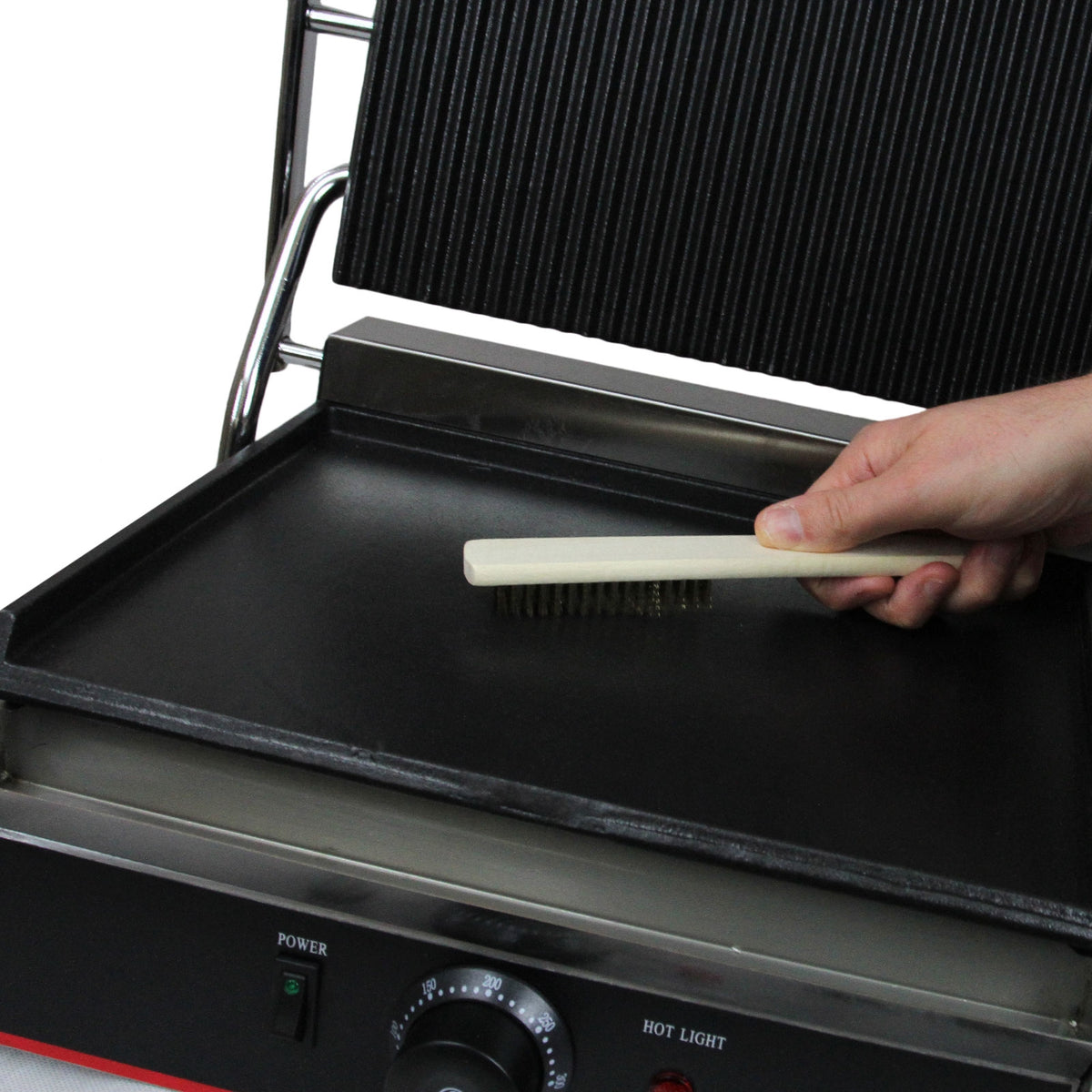 Edelstahl Panini Grill mit einer glatten und einer gerillten Fläche, Hand mit Bürste reinigt die Oberfläche, glänzende Textur und robuste Bauweise