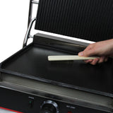 Edelstahl Panini Grill mit einer glatten und einer gerillten Fläche, Hand mit Bürste reinigt die Oberfläche, glänzende Textur und robuste Bauweise