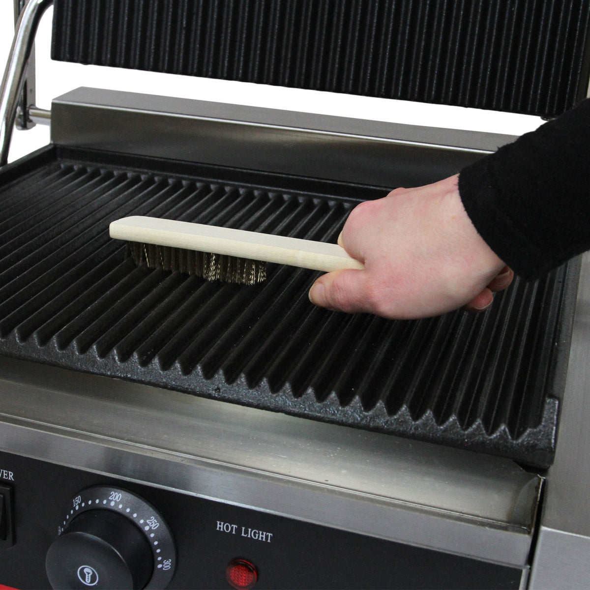 Ein Handgriff mit einer Holzbürste reinigt die geriffelte Grillfläche des KuKoo Panini Grills, der aus robustem Edelstahl gefertigt ist