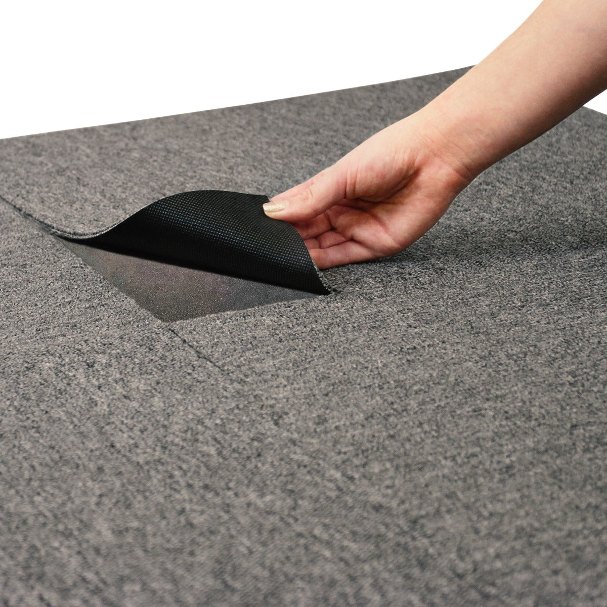 Anthrazitfarbene Teppichfliese 50 x 50 cm mit strukturiertem Obermaterial, eine Hand hebt die Fliese an, um die Unterseite zu zeigen, ideal für Bodenbeläge