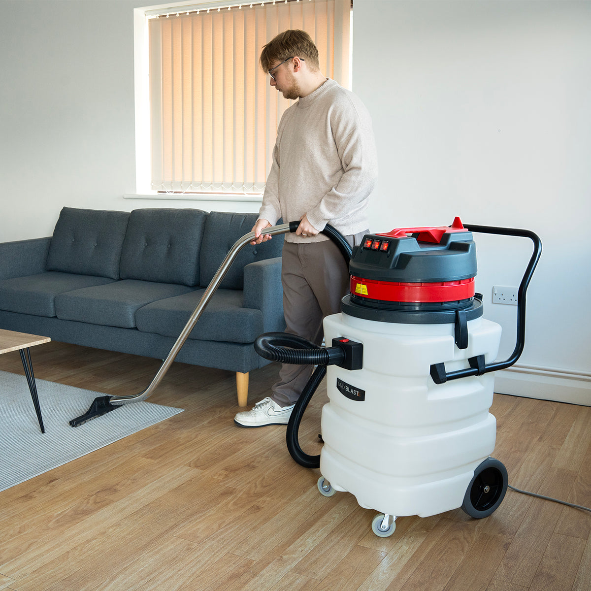 Industriesauger Maxblast 90L in Weiß mit rotem Deckel, der von einer Person in einem modernen Raum mit Holzfußboden verwendet wird