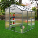 Gewächshaus 1.8m x 1.8m ohne Boden aus transparentem Polycarbonat, mit stabilen Metallrahmen und Regalen für Pflanzen, umgeben von grünem Gras und Bäumen