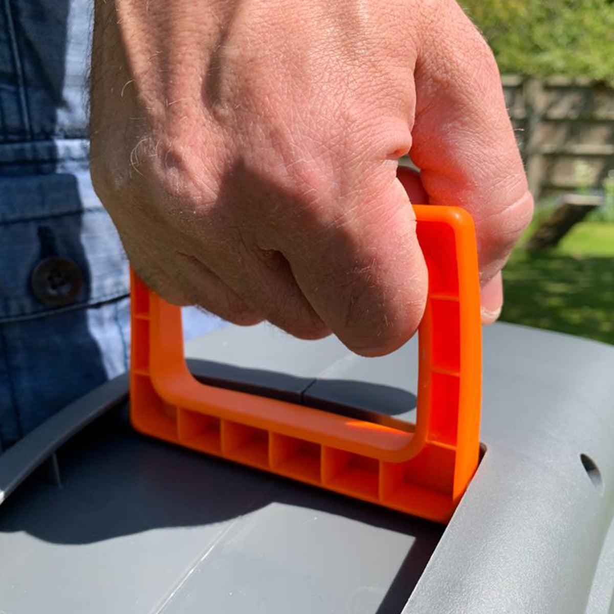 Hand hält den orangefarbenen Griff einer 30m Schlauchtrommel, die auf einer grauen Oberfläche platziert ist, im Garten mit grünem Hintergrund