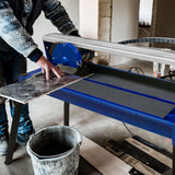 Fliesenschneider mit blauem Tisch, 720mm, 800W, Benutzer schneidet eine dunkle Fliese, robuste Bauweise und präzise Klinge sichtbar