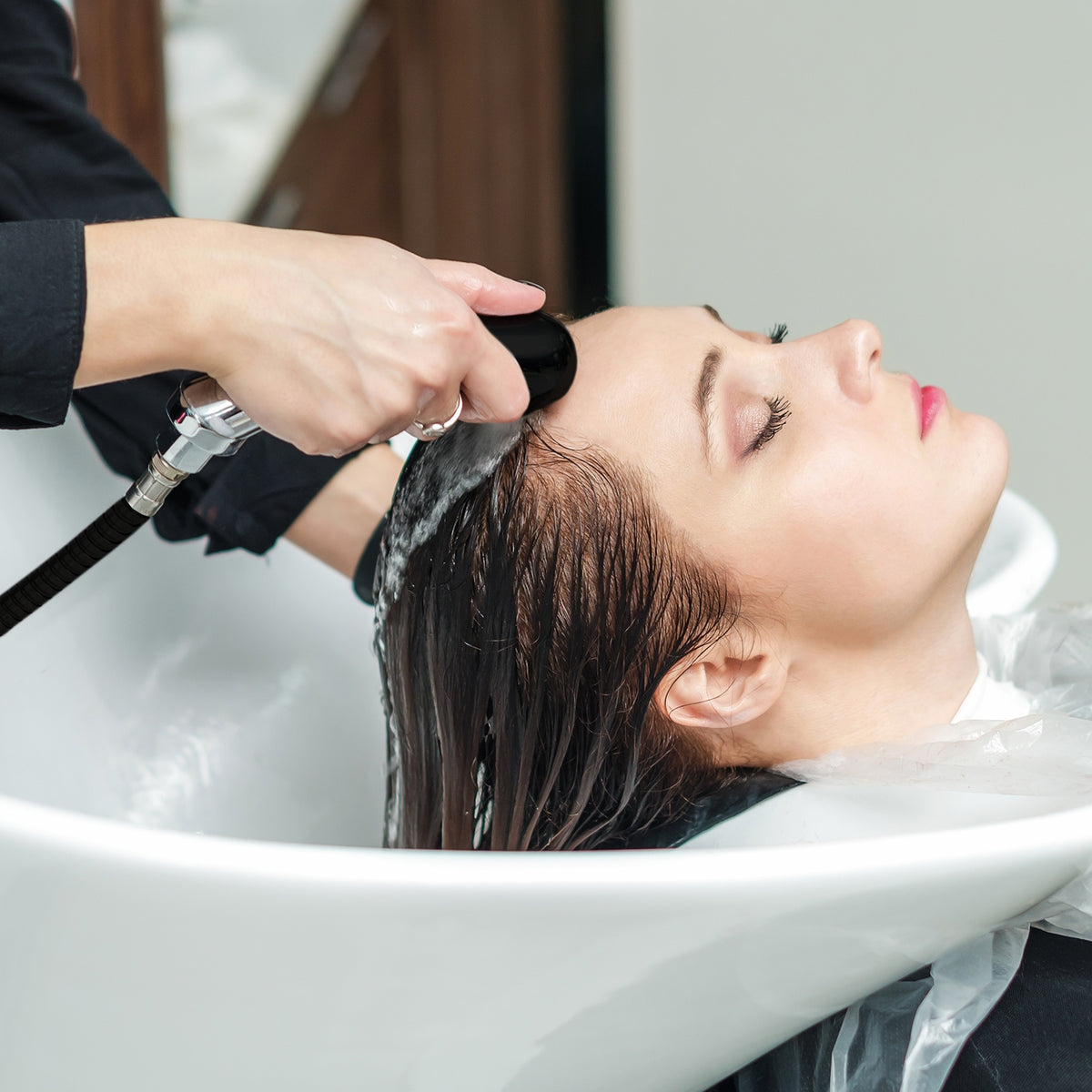 Eleganter Friseurwaschsessel in Weiß, mit einer Kundin, die eine Haarwäsche erhält, sanfte Wasserstrahlen und gepflegte, glänzende Haare