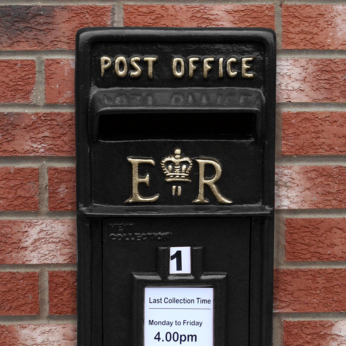 Schwarzer Briefkasten im englischen Stil mit goldenen Buchstaben "POST OFFICE" und "ER", verziert mit einer Krone, vor rotem Backsteinmauerwerk