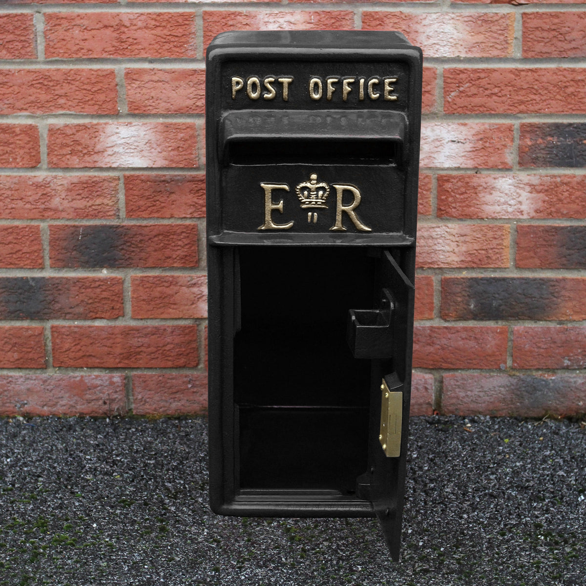 Schwarzer Briefkasten mit Bodenständer, dekoriert mit goldenen Buchstaben "POST OFFICE" und "ER", aus robustem Metall, vor einer Backsteinmauer