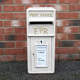Weißer Briefkasten im englischen Stil mit goldenen Buchstaben, auf einem grauen Untergrund, umgeben von roten Ziegelsteinen und einem Informationsschild