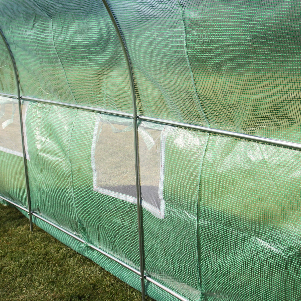 Transparenter Polytunnel aus grünem, strapazierfähigem Material mit belüftenden Fenstern, ideal für den Anbau von Pflanzen im Garten