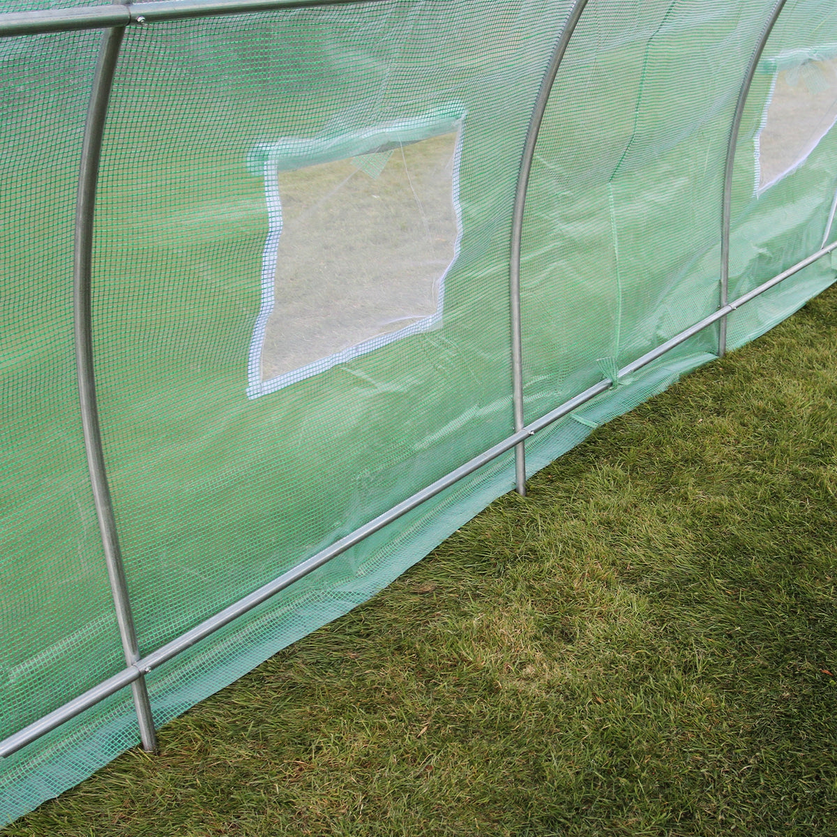 Grüner Polytunnel aus 25mm Metallrahmen mit Netzfenstern, ideal für Pflanzenanbau, auf grünem Grasboden platziert, bietet Schutz und Belüftung