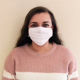 Eine Frau trägt eine weiße, eng anliegende Gesichtmaske aus weichem Material, kombiniert mit einem rosa gestreiften Pullover, vor einem neutralen Hintergrund