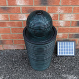 Schwarzer Kugelbrunnen mit strukturiertem, gewelltem Design, umgeben von Ziegelwand und Solar-Panel, ideal für Garten oder Terrasse