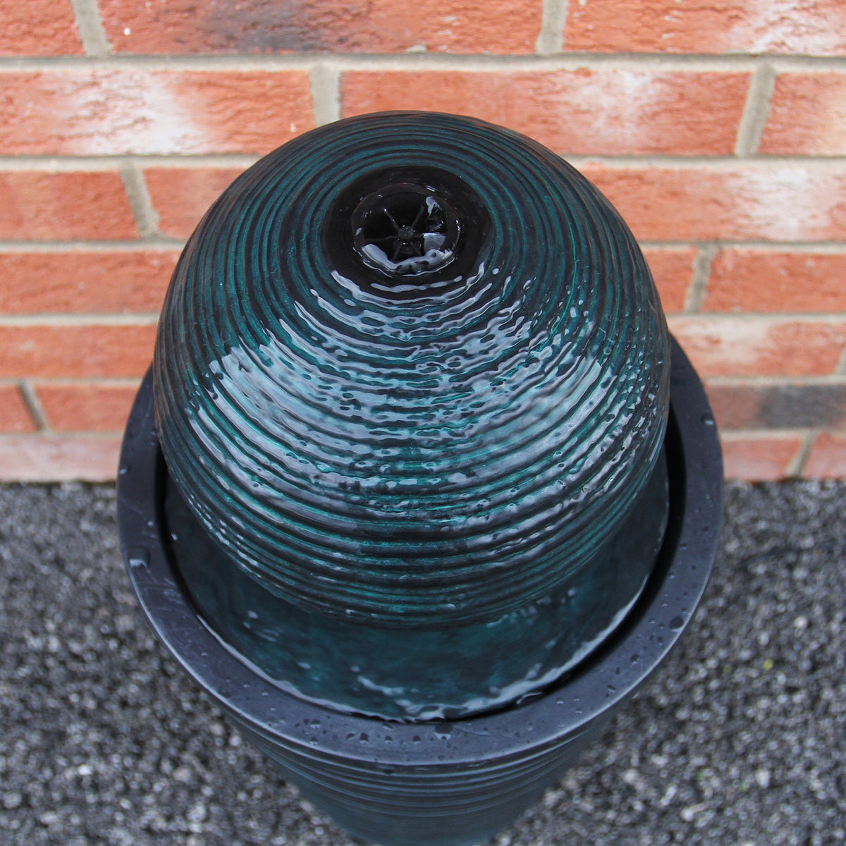 Schwarzer Kugelbrunnen mit gewellter Oberfläche, der Wasser sanft aus der Spitze sprudelt, umgeben von einem runden, mattschwarzen Behälter