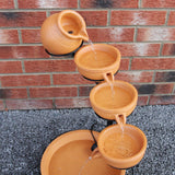 Terracotta Solar Kaskadenbrunnen mit vier Schalen, die Wasser in eine große Schale leiten, umgeben von grauem Kies und einer roten Ziegelmauer
