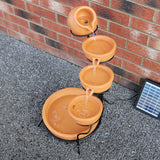 Terracotta Solar Kaskadenbrunnen mit vier Schalen, Wasser fließt sanft von oben nach unten, umgeben von einem stabilen Metallgestell und einem Solarpanel