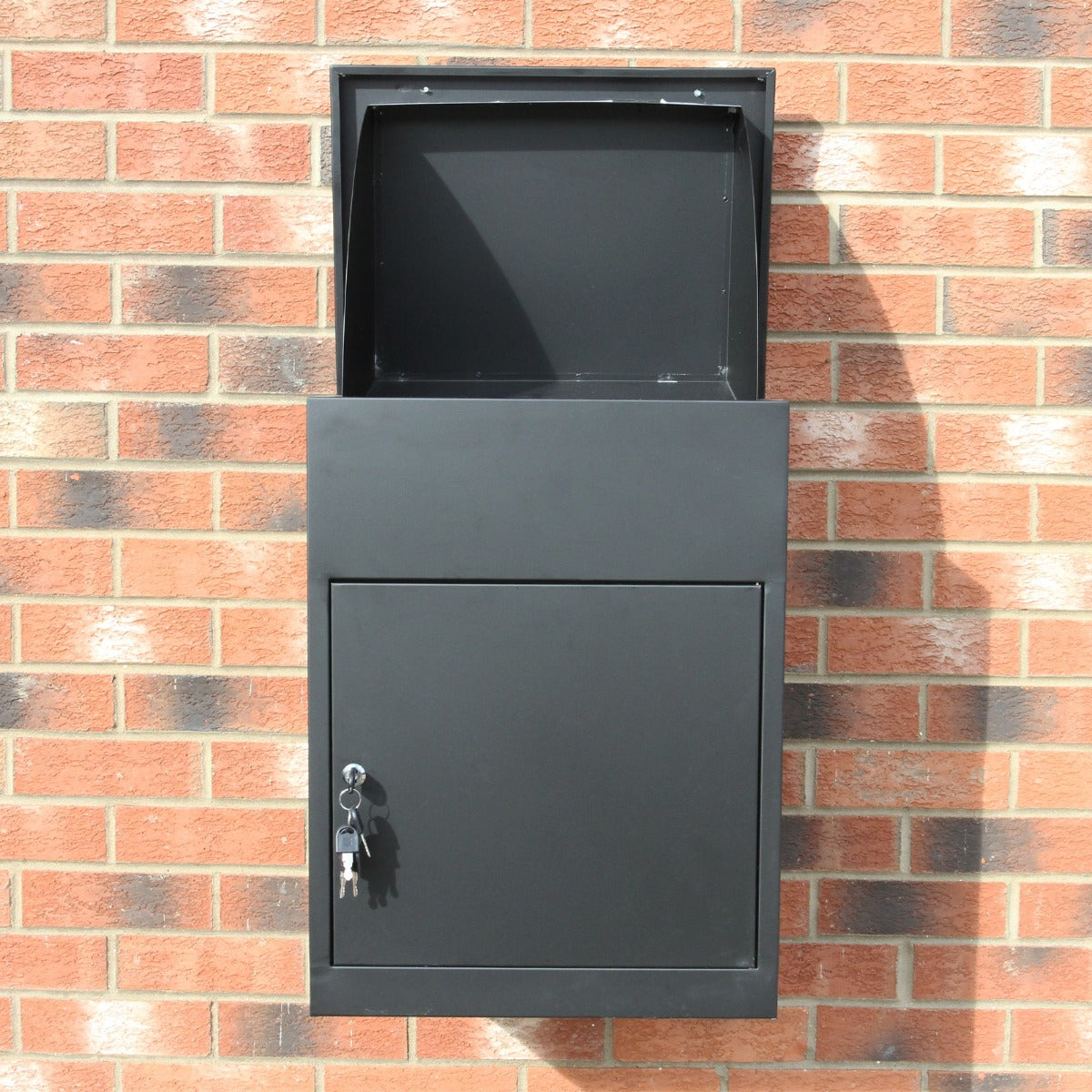 Schwarzer Paketkasten aus robustem Metall mit abschließbarem Fach, montiert an einer Ziegelwand, ideal für die sichere Zustellung von Paketen