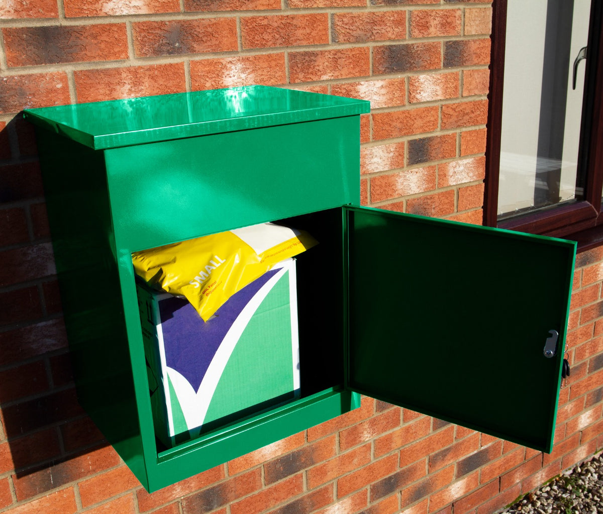 Grüner Paketkasten aus robustem Metall, an einer Ziegelwand montiert, mit offenem Deckel und sichtbarem Paket in gelber und grüner Verpackung