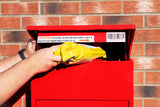 Roter Paketkasten aus robustem Metall, geöffnet, während ein gelbes Paket hineingelegt wird, vor einer gemusterten Ziegelwand