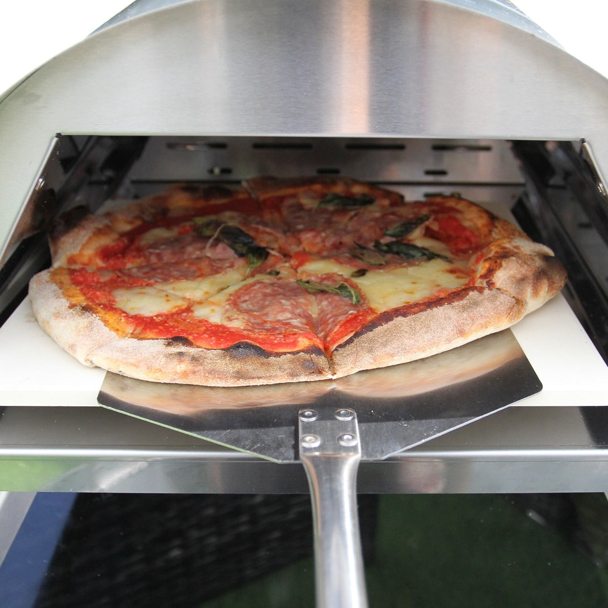 Ein frisch gebackene Pizza mit knusprigem Rand, belegt mit Tomatensauce, Käse, Salami und frischem Basilikum, im Tisch-Pizzaofen sichtbar