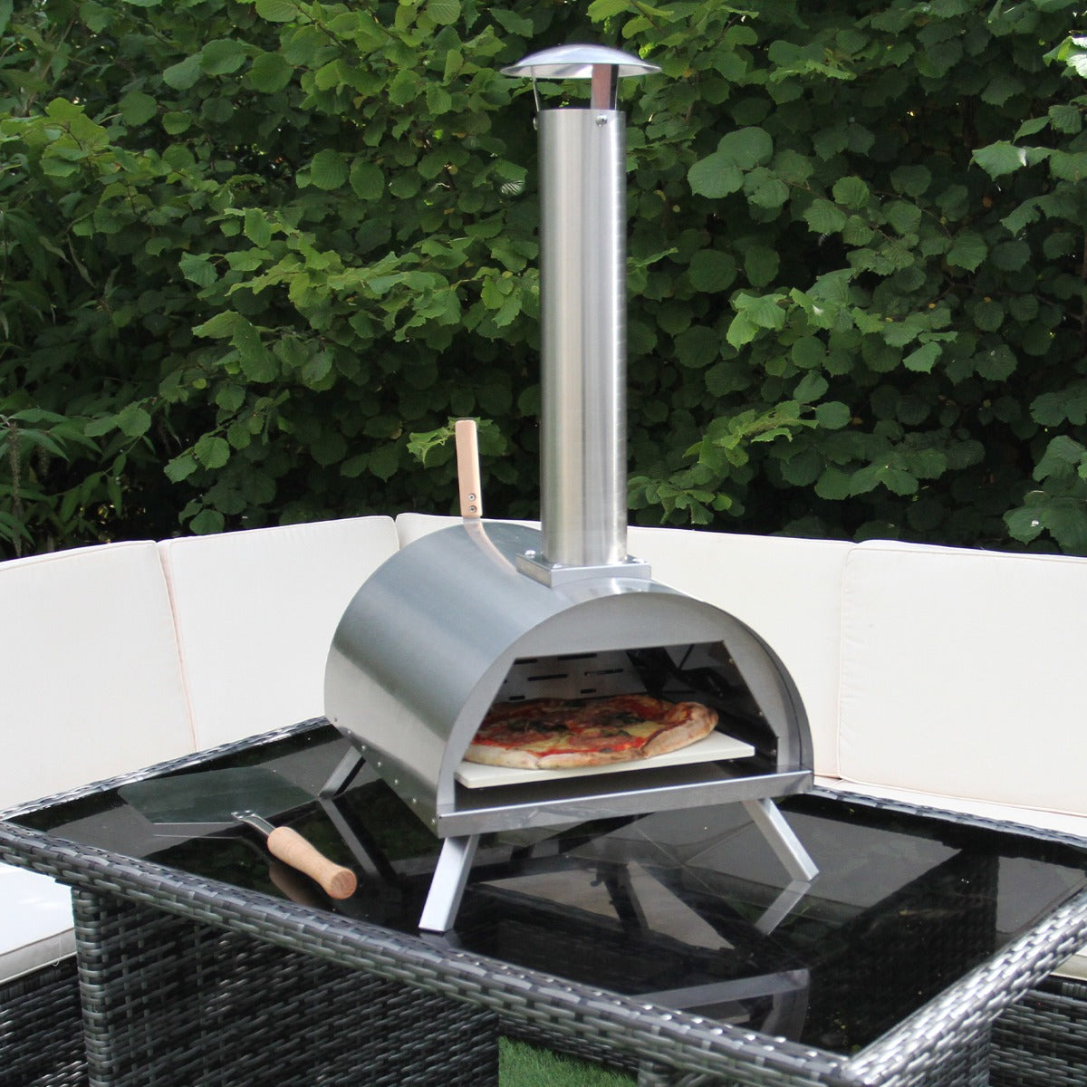Kompakter Tisch-Pizzaofen aus Edelstahl mit einem glänzenden, silbernen Finish, der auf einem modernen Tisch steht und eine frisch gebackene Pizza zeigt