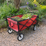 Faltbarer Gartenwagen in leuchtendem Rot mit stabilen schwarzen Rädern, gefüllt mit bunten Pflanzen, steht auf einem Kiesweg umgeben von Blumenbeeten
