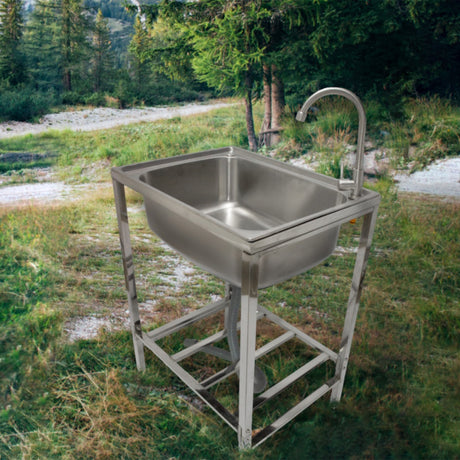 Edelstahl Camping-Spüle auf einem stabilen Gestell, glänzende Oberfläche, rechteckige Form, ideal für den Einsatz im Freien, umgeben von Natur