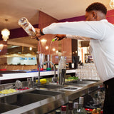 Elegante KuKoo Doppel Cocktail-Bar Station mit Edelstahl-Oberfläche, Gläsern, frischen Zutaten und einem Barkeeper, der Cocktails zubereitet
