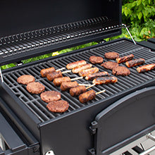 Saftige Burger-Patties und gegrillte Spieße auf einem schwarzen Grillrost, umgeben von frischem Grün im Hintergrund