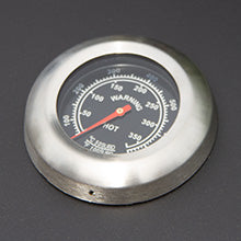 Ein runder, silberner Temperaturmesser mit schwarzem Ziffernblatt und rotem Zeiger, der Temperaturen bis 350 Grad anzeigt, auf dunklem Hintergrund
