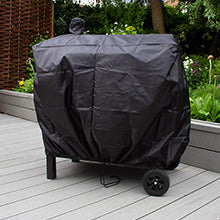 Schwarze, wetterfeste Abdeckung für einen Grill, mit robustem Material und praktischen Rollen, auf einer Holzterrasse mit grünen Pflanzen im Hintergrund