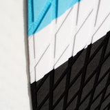 Detailansicht des blauen aufblasbaren Paddle Boards mit strukturiertem Griff, diagonalen Farbstreifen in Blau, Weiß und Schwarz, ideal für Wassersport